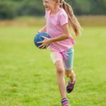 girl in pink tank top and pink shorts holding blue soccer ball